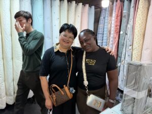 Two women posing and smiling together inside a bustling textile and bedding shop